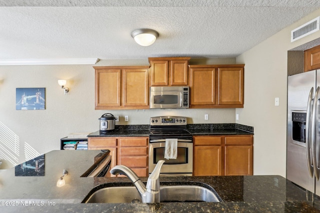 kitchen with dark stone countertops, appliances with stainless steel finishes, sink, and a textured ceiling