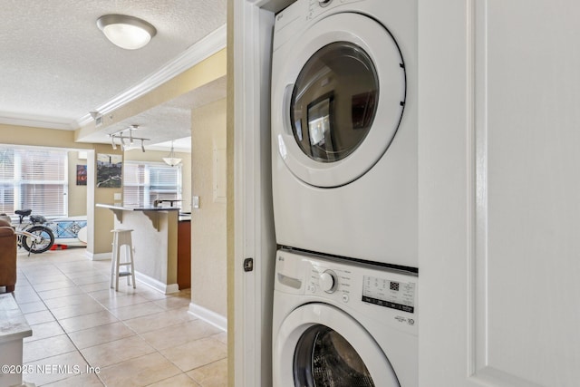 laundry room with a textured ceiling, stacked washing maching and dryer, crown molding, and light tile patterned floors