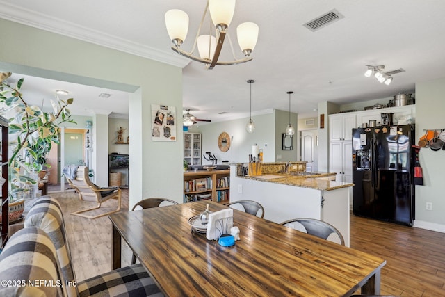 dining room featuring ceiling fan with notable chandelier, visible vents, crown molding, and wood finished floors