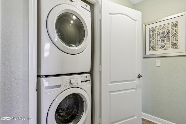 washroom featuring stacked washer / drying machine, laundry area, a textured wall, and baseboards