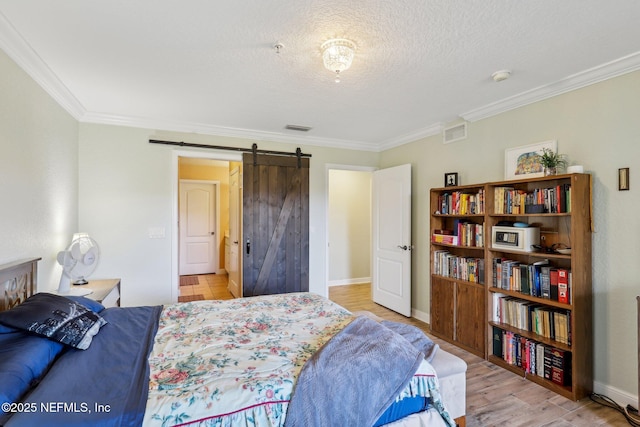 bedroom featuring a textured ceiling, a barn door, visible vents, ornamental molding, and light wood finished floors