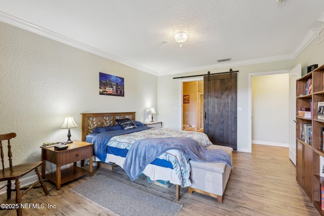 bedroom with a barn door, light wood-style flooring, visible vents, baseboards, and ornamental molding