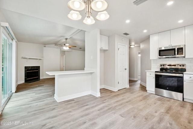 kitchen featuring appliances with stainless steel finishes, white cabinetry, decorative backsplash, hanging light fixtures, and light hardwood / wood-style flooring