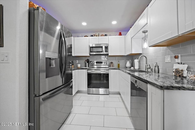 kitchen with sink, white cabinetry, dark stone counters, stainless steel appliances, and decorative backsplash