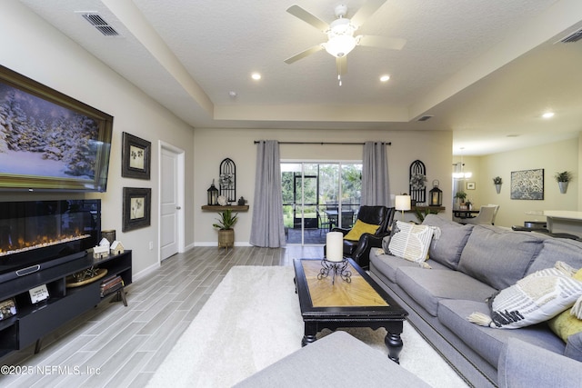 living room with visible vents, baseboards, wood tiled floor, a tray ceiling, and a glass covered fireplace