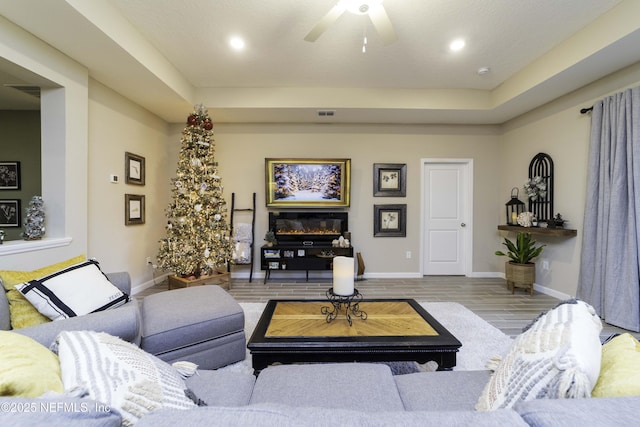 living area featuring a tray ceiling, recessed lighting, light wood-style floors, a ceiling fan, and baseboards