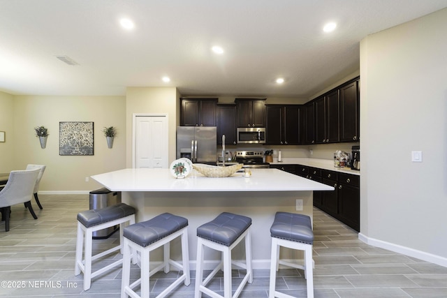 kitchen with a kitchen island with sink, a breakfast bar, visible vents, light countertops, and appliances with stainless steel finishes