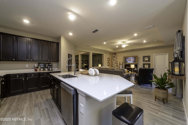 kitchen featuring a sink, visible vents, light countertops, dishwasher, and an island with sink