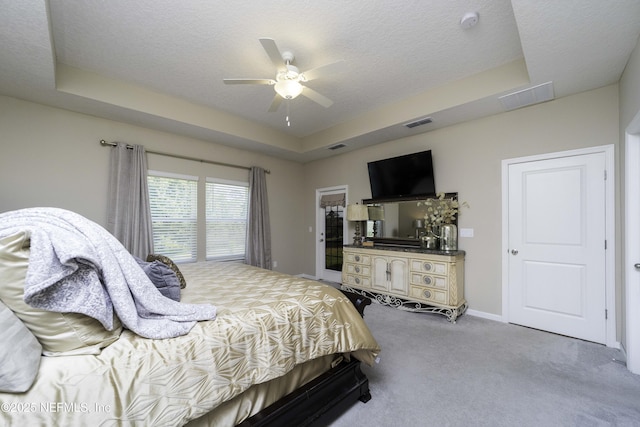 bedroom with carpet floors, a tray ceiling, visible vents, and a textured ceiling