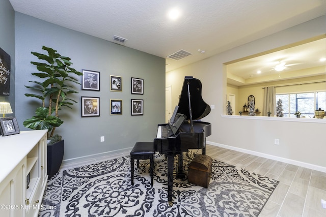 sitting room with light wood-type flooring, baseboards, visible vents, and a textured ceiling