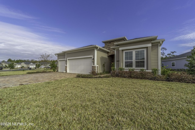 prairie-style home featuring a garage, stone siding, decorative driveway, and a front yard