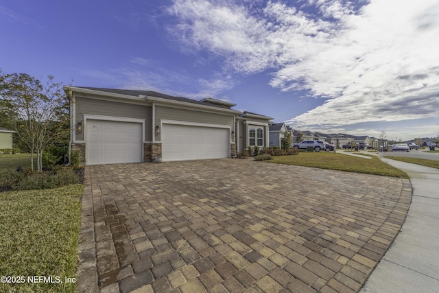 view of front facade with a garage, stone siding, decorative driveway, and a front yard