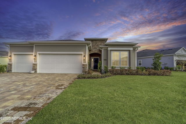 prairie-style home with decorative driveway, stone siding, a lawn, and an attached garage