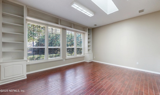 empty room with dark hardwood / wood-style floors, lofted ceiling with skylight, and built in features