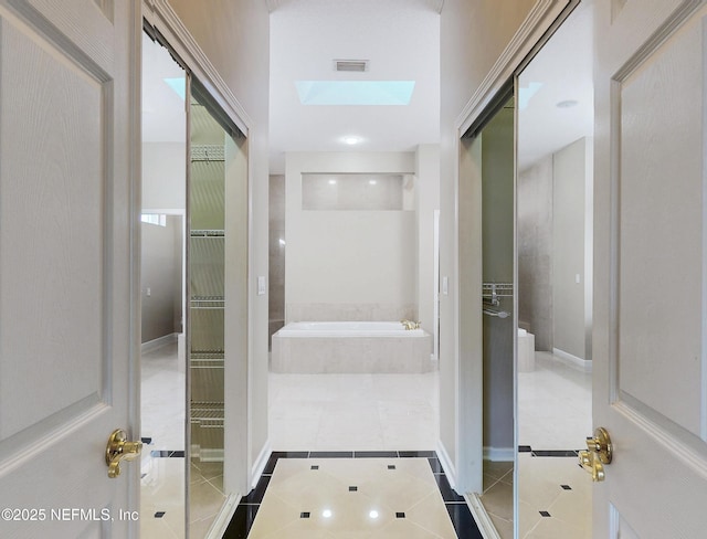 bathroom with a relaxing tiled tub, a skylight, and tile patterned flooring