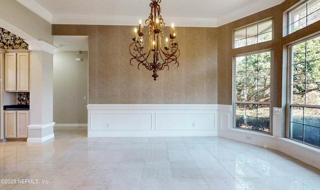 spare room with decorative columns, crown molding, and an inviting chandelier