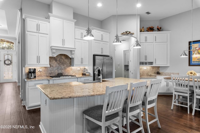 kitchen featuring white cabinetry, decorative light fixtures, stainless steel appliances, and an island with sink