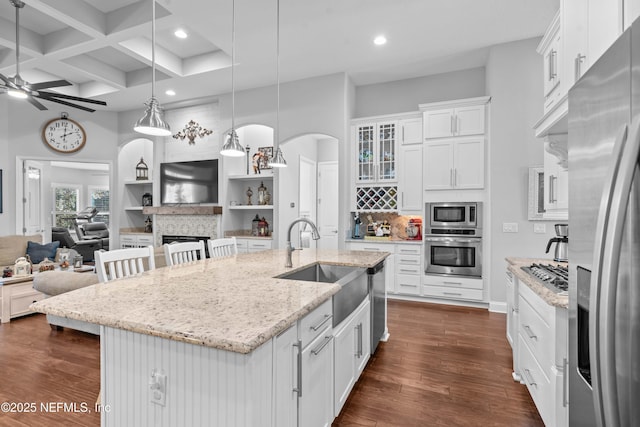 kitchen with sink, appliances with stainless steel finishes, hanging light fixtures, an island with sink, and white cabinets