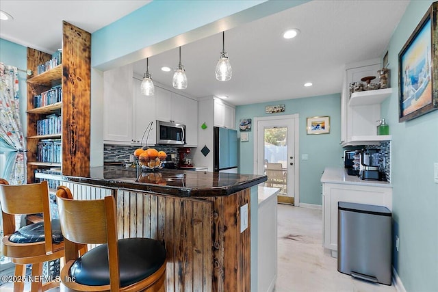 kitchen featuring black refrigerator, tasteful backsplash, white cabinets, hanging light fixtures, and kitchen peninsula