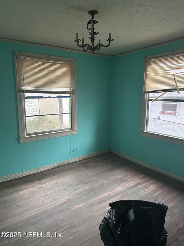 empty room with wood-type flooring, a notable chandelier, and a textured ceiling