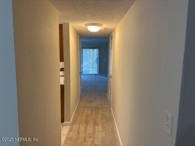 hall with light carpet and a textured ceiling