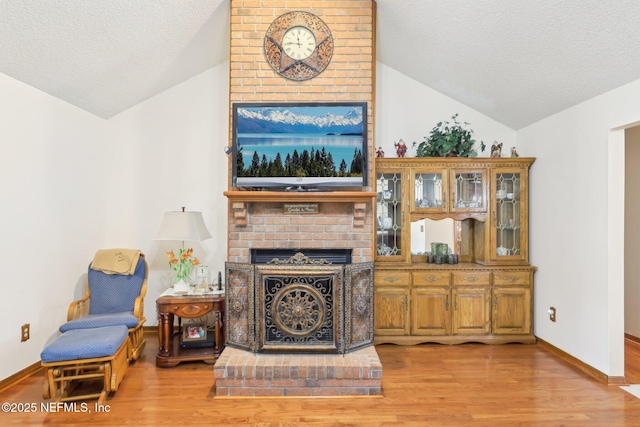 living room with lofted ceiling, a brick fireplace, light hardwood / wood-style flooring, and a textured ceiling