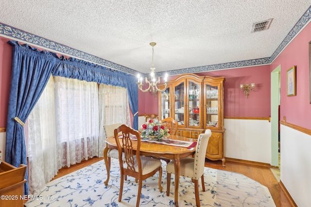 dining space featuring a notable chandelier, a textured ceiling, and light wood-type flooring