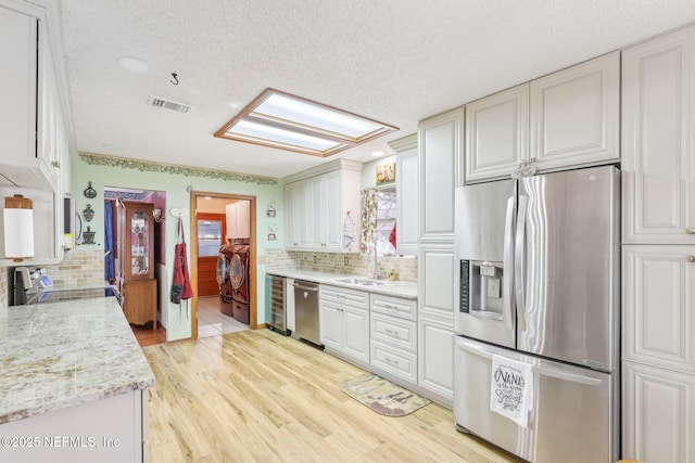 kitchen featuring stainless steel appliances, washing machine and dryer, light stone countertops, and white cabinets