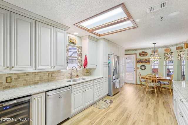 kitchen with sink, appliances with stainless steel finishes, hanging light fixtures, wine cooler, and white cabinets