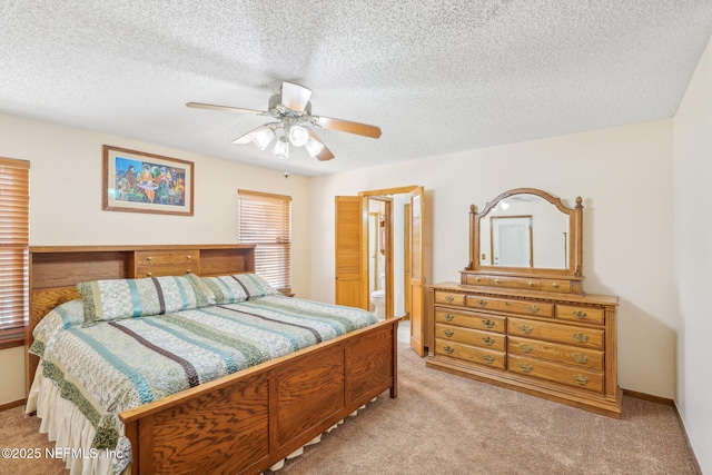 bedroom with ceiling fan, light colored carpet, ensuite bathroom, and a textured ceiling