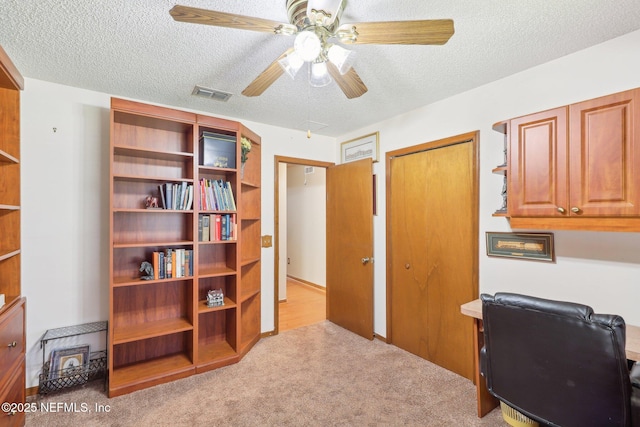 home office featuring ceiling fan, light carpet, and a textured ceiling