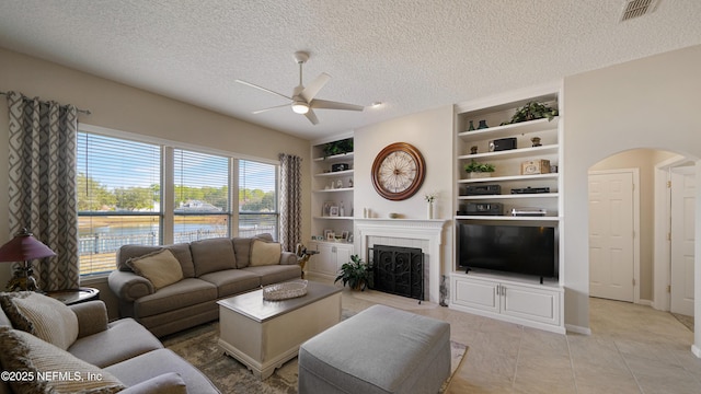 tiled living room featuring built in shelves, ceiling fan, and a textured ceiling