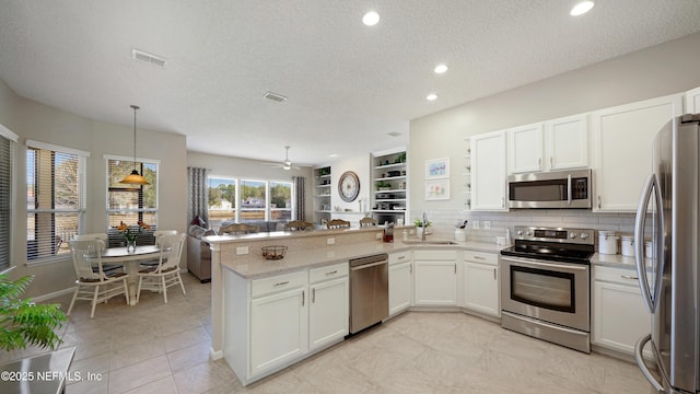 kitchen featuring appliances with stainless steel finishes, pendant lighting, white cabinets, and kitchen peninsula