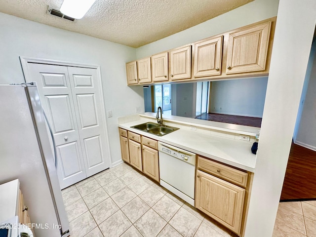 kitchen with light tile patterned flooring, sink, light brown cabinets, fridge, and dishwasher