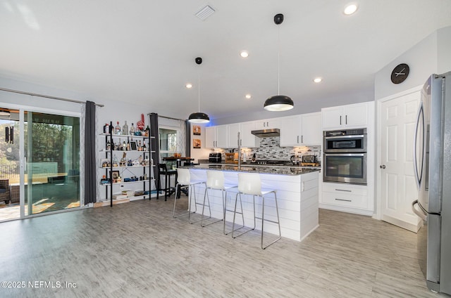 kitchen featuring white cabinetry, a center island, hanging light fixtures, dark stone counters, and stainless steel appliances