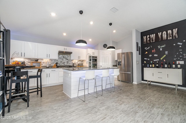 kitchen with white cabinetry, stainless steel appliances, an island with sink, and dark stone countertops