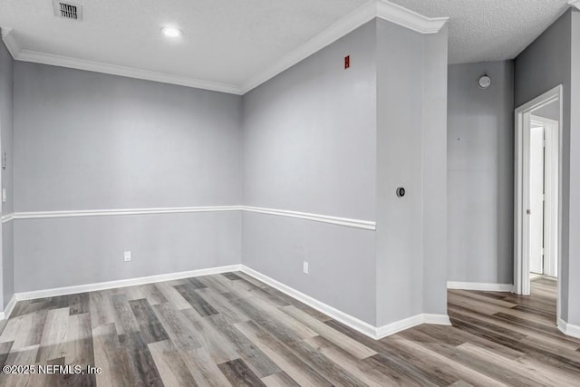 spare room with baseboards, visible vents, ornamental molding, wood finished floors, and a textured ceiling