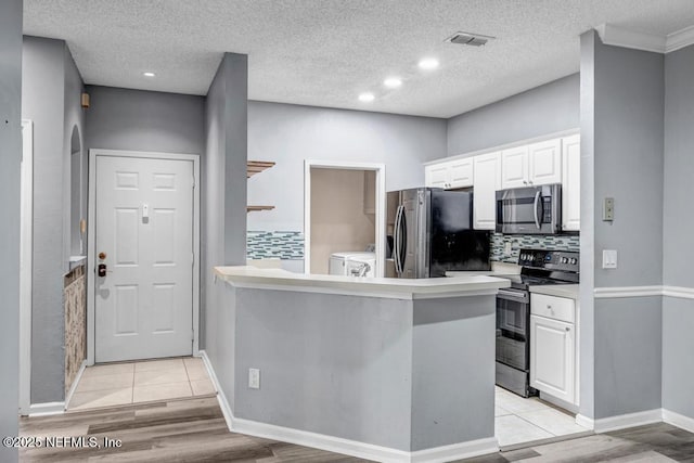 kitchen featuring light countertops, appliances with stainless steel finishes, white cabinetry, washer and dryer, and a peninsula