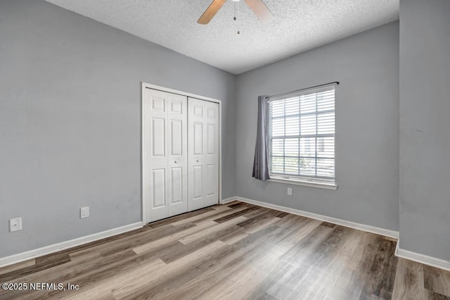 unfurnished bedroom featuring a textured ceiling, light wood-style flooring, a ceiling fan, baseboards, and a closet