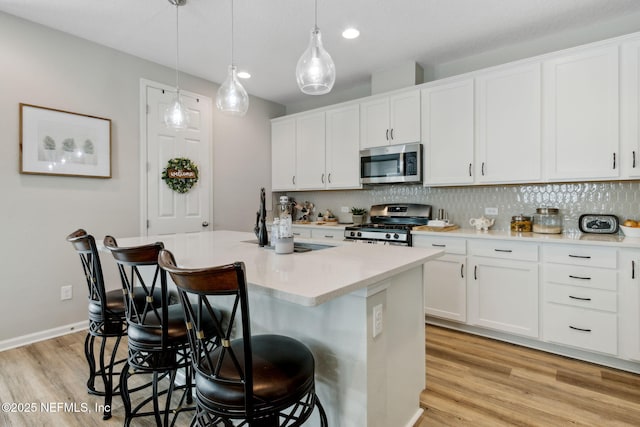 kitchen featuring decorative light fixtures, white cabinetry, a kitchen bar, a kitchen island with sink, and stainless steel appliances