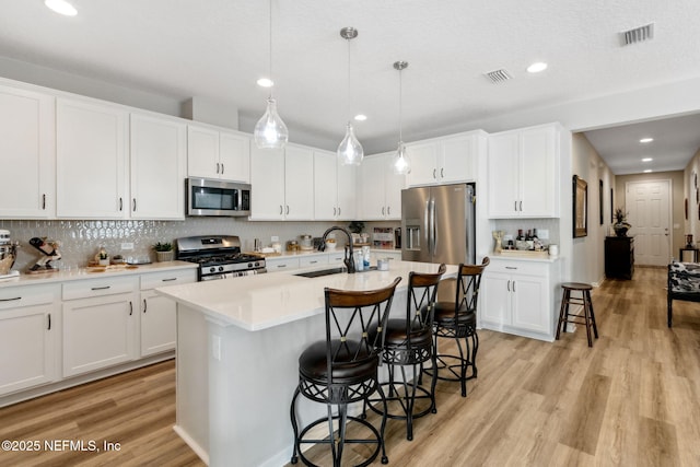 kitchen with sink, white cabinetry, hanging light fixtures, stainless steel appliances, and an island with sink