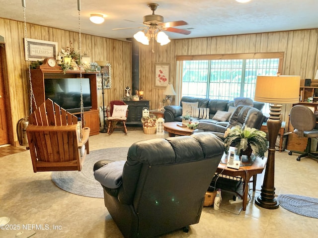 living room featuring ceiling fan, a wood stove, and wooden walls