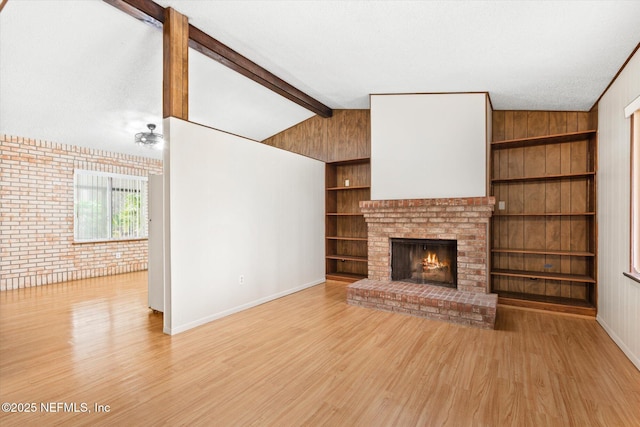 unfurnished living room featuring vaulted ceiling with beams, light hardwood / wood-style flooring, built in features, and brick wall