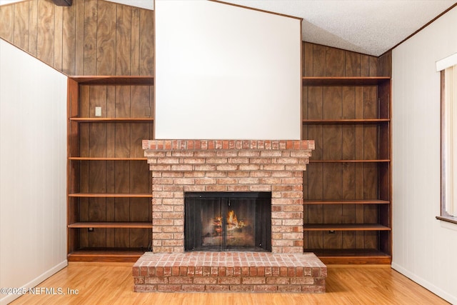 unfurnished living room with built in shelves, wood-type flooring, a fireplace, and a textured ceiling