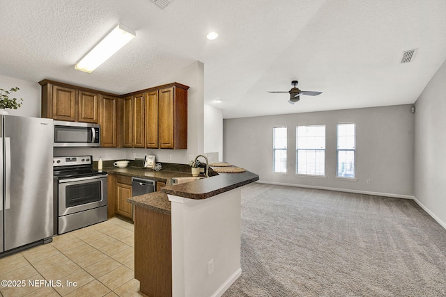 kitchen with sink, stainless steel appliances, a textured ceiling, light carpet, and kitchen peninsula