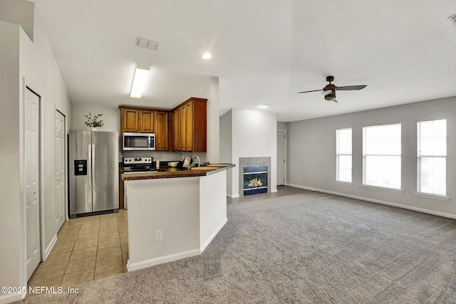 kitchen featuring a tile fireplace, appliances with stainless steel finishes, kitchen peninsula, light carpet, and a textured ceiling