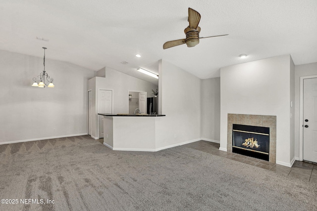 unfurnished living room with ceiling fan with notable chandelier, lofted ceiling, carpet flooring, a tiled fireplace, and a textured ceiling