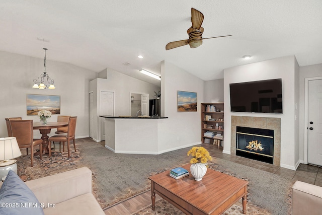 living room featuring ceiling fan with notable chandelier, a fireplace, vaulted ceiling, and a textured ceiling