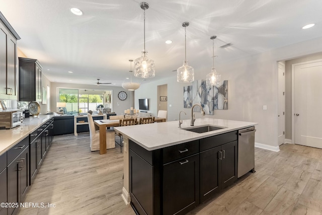 kitchen with sink, hanging light fixtures, a center island with sink, stainless steel dishwasher, and light hardwood / wood-style floors