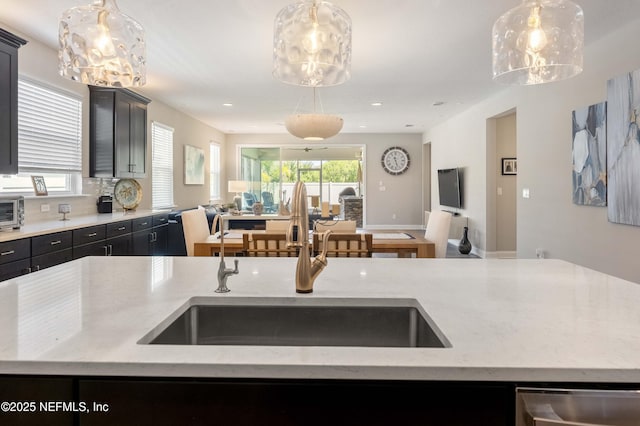 kitchen with sink, light stone countertops, a kitchen island with sink, and hanging light fixtures